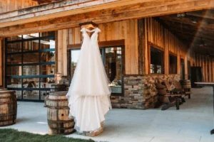 Kaitlin’s elegant wedding dress hangs gracefully from the rustic barn wall at Whispering Pines.