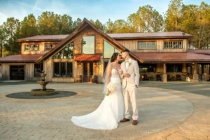 Bride Madison and groom Dylan pose in front of Whispering Pine Venue’s rustic barn