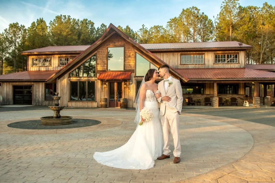 Bride Madison and groom Dylan pose in front of Whispering Pine Venue’s rustic barn