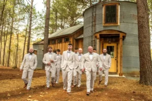Groomsmen in light gray suits walk together outside Whispering Pine Event Venue’s rustic silo