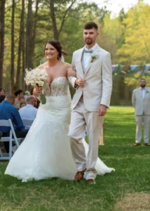 Bride Madison in a white lace gown and groom Dylan in a light gray suit walk arm-in-arm during their outdoor ceremony