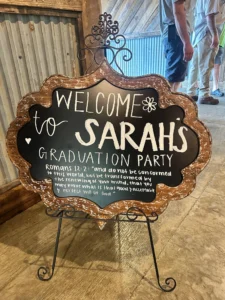 A chalkboard sign on a stand welcoming guests to Sarah’s graduation party.
