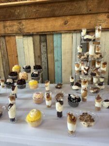 A dessert table at Sarah’s graduation party with cupcakes and parfaits on a multi-tiered display, set against a weathered wooden backdrop with purple and white accents.