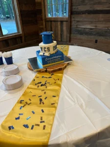 A multi-tiered cake at Peyton’s graduation party with a graduation cap topper, decorated in blue and yellow.