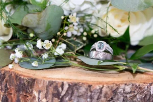Close-up of wedding rings displayed on a wood slice with white flowers, greenery, and eucalyptus accents.