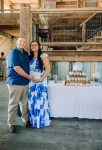 A beautifully decorated dessert table with a multi-tiered stand of blue and white cupcakes, flowers, and a rustic wooden background at Whispering Pines Venue during Rebecca and Dylan's baby shower.
