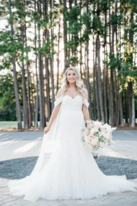 Callie posing gracefully in her bridal portrait at Whispering Pines Venue, with the rustic backdrop of pine trees enhancing her timeless beauty.