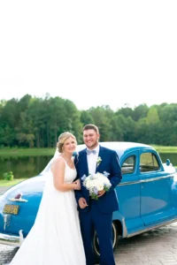 Newlywed couple posing in front of a vintage blue antique car at Whispering Pines Venue, celebrating their wedding day.