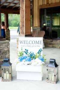 Wedding reception welcome sign at Whispering Pines Venue featuring elegant floral accents and Carolina blue details.