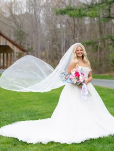 Bride Zoey Elliott twirls in her wedding dress on the manicured lawn in front of the rustic covered bridge at Whispering Pines Venue in Henderson, NC.