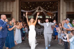Newly married couple celebrating their wedding with a joyful bubble exit outside the barn reception at Whispering Pines Venue in Henderson, NC.