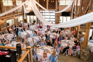 Guests gathered for Chris and Lana's wedding reception inside Whispering Pines Venue, featuring elegant white drapery, string lights, and rustic barn architecture.