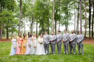 Bride and groom pose with their bridesmaids and groomsmen in the wooded grounds at Whispering Pines Venue.